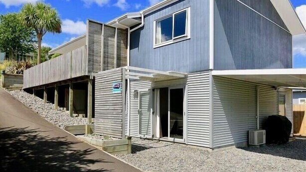 Una casa moderna de dos pisos con fachada gris, un ventanal grande en el segundo nivel y un porche cubierto.