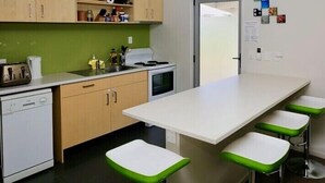 Una cocina moderna con encimera blanca, taburetes de bar verdes y armarios de madera.