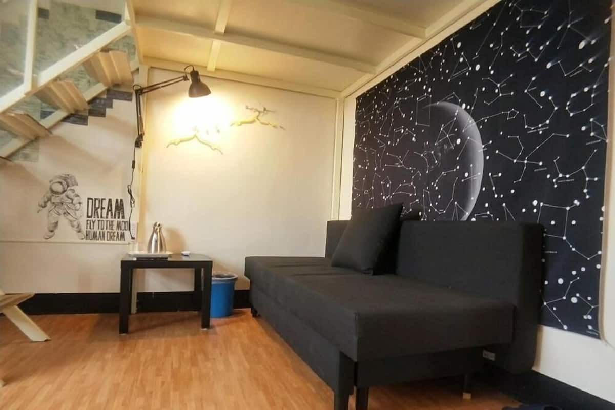 A modern living room with a dark sofa, a small side table, a lamp, and a wall with a celestial design.