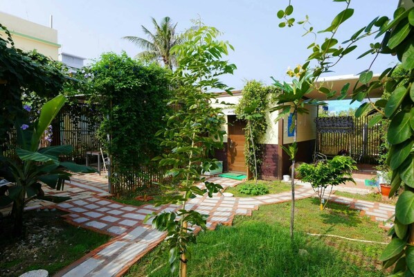 A courtyard with a checkered tile pathway, lush greenery, and a building with a wooden door. - Fan Zai Cuo (Liuqiu)