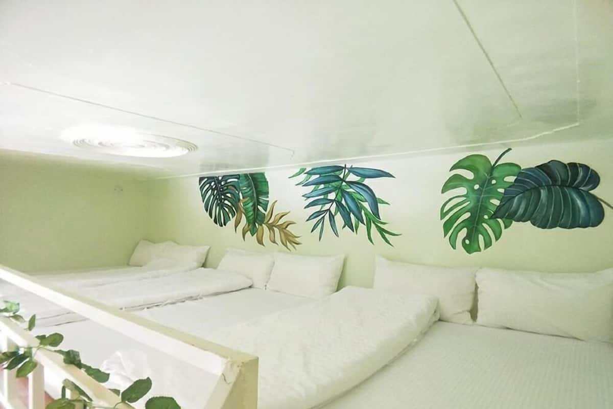 A room with a bed, a small table, and a wall with tropical leaf art.