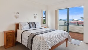 Une chambre à coucher avec un lit, une table de chevet, une fenêtre et un balcon donnant sur la mer.