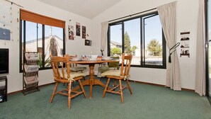 A dining area with a round table and four chairs, large windows with curtains, and a green carpet.