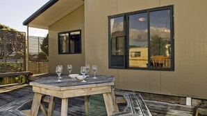 A wooden deck with a table set for dining, a covered seating area, and a building with large windows.
