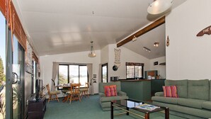 A living room with a green sofa, a wooden coffee table, and a television. There is a dining area with a table and chairs.