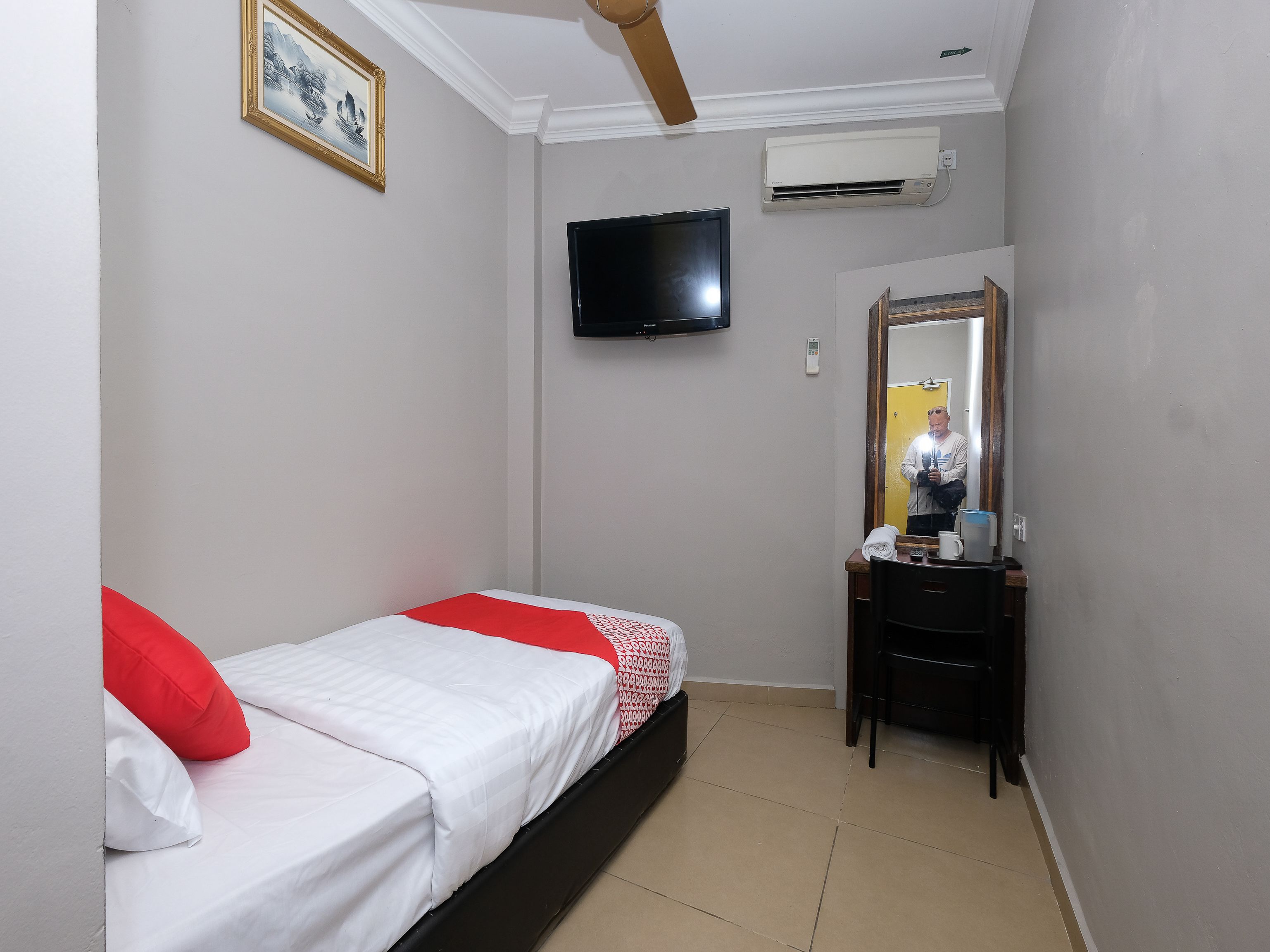 A bedroom with a bed, a TV, an air conditioner, a mirror, and a desk.