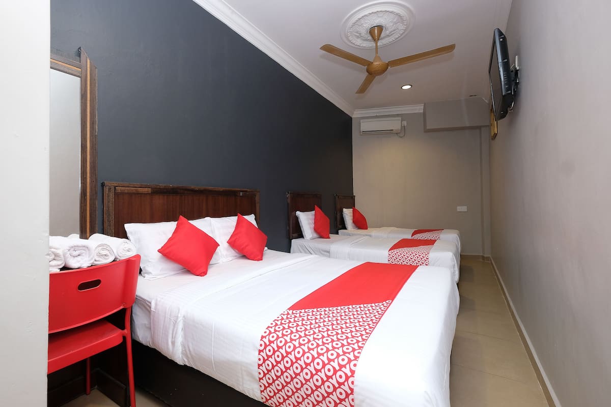 Ein Hotelzimmer mit zwei Betten, rot-weiß gestreifter Bettwäsche, einem Deckenventilator und einem an der Wand befestigten Fernseher.