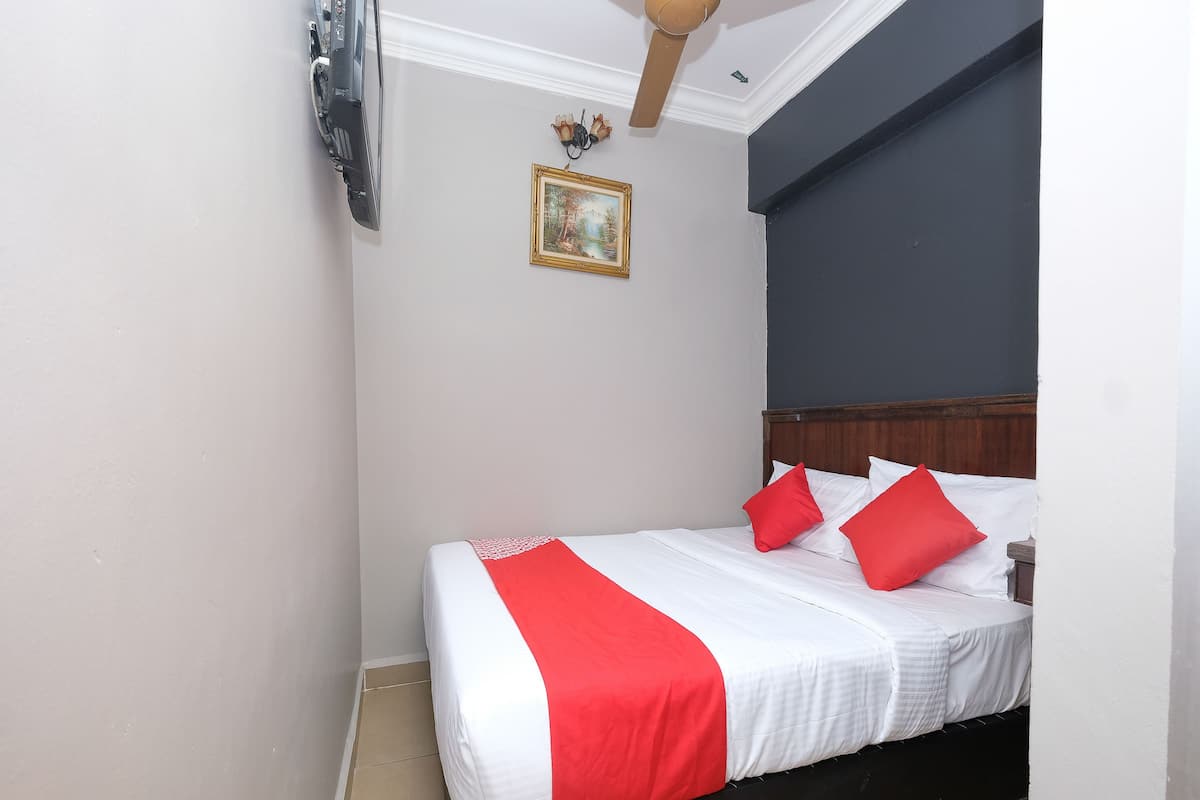 Ein ordentlich bezogenes Bett mit weißer und roter Bettwäsche, ein hölzerner Kopfteil und ein kleines gerahmtes Bild an der Wand.