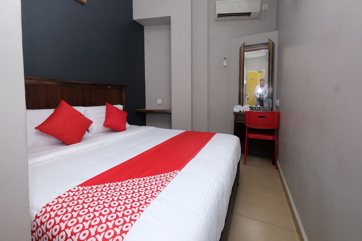 Ein Hotelzimmer mit einem Bett, einem roten Sessel, einem Schreibtisch und einem Spiegel.