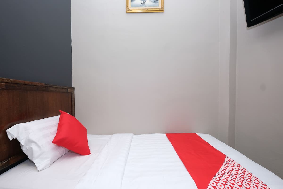 Ein Einzelbett mit weißer Bettwäsche und einer Decke mit roten und weißen Mustern.