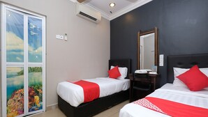 Ein Hotelzimmer mit zwei Betten, beide mit weißer Bettwäsche und roten Akzenten, einem Deckenventilator, einer Klimaanlage, einem großen Spiegel und Blick auf eine tropische Szenerie durch eine Glastür.