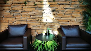 Une pièce avec un mur en pierre, deux fauteuils en cuir, une table ronde ornée d’une plante verte et une bouteille posée sur la table.
