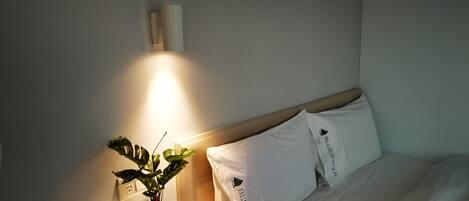 Ein Hotelzimmer mit einem Bett, weißen Kissen, einem Nachttisch mit Pflanze und einer Wandleuchte.