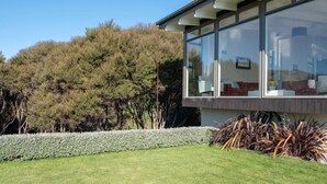 A modern building with large windows, a well-maintained lawn, and a variety of plants. - Kotare Point Paradise - Akaroa Holiday Home (Akaroa)
