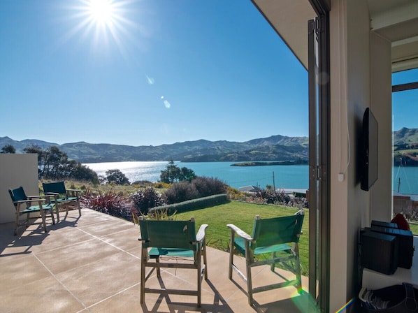 A balcony with a view of a lake and mountains, two green chairs, and a TV mounted on the wall.