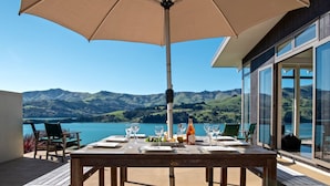 A wooden deck with a table set for dining, overlooking a lake and mountains. - Kotare Point Paradise - Akaroa Holiday Home (Akaroa)