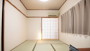 A traditional Japanese room with tatami flooring, a sliding shoji door, and a ceiling-mounted air conditioner. - U-SHUKU Osaka (Osaka)
