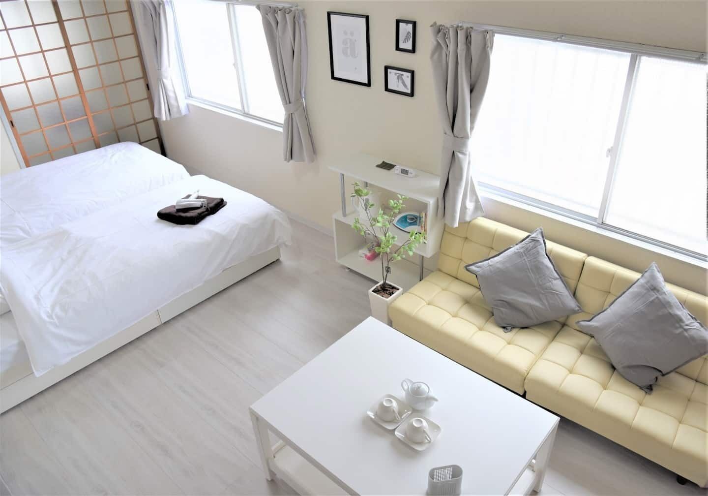 A modern hotel room with a bed, a sofa, a coffee table, and a small plant.