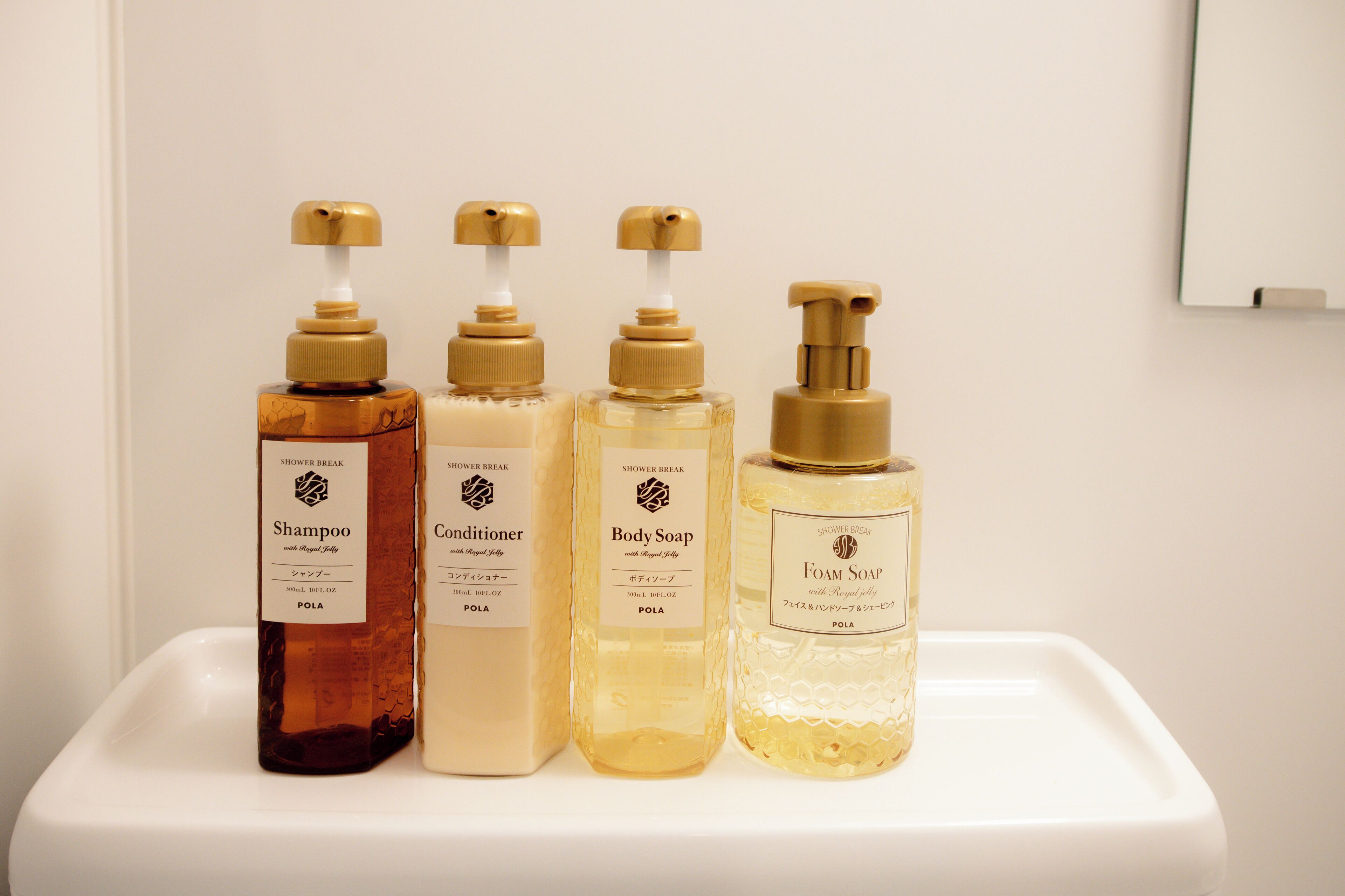 Four bottles of shower products on a white shelf.