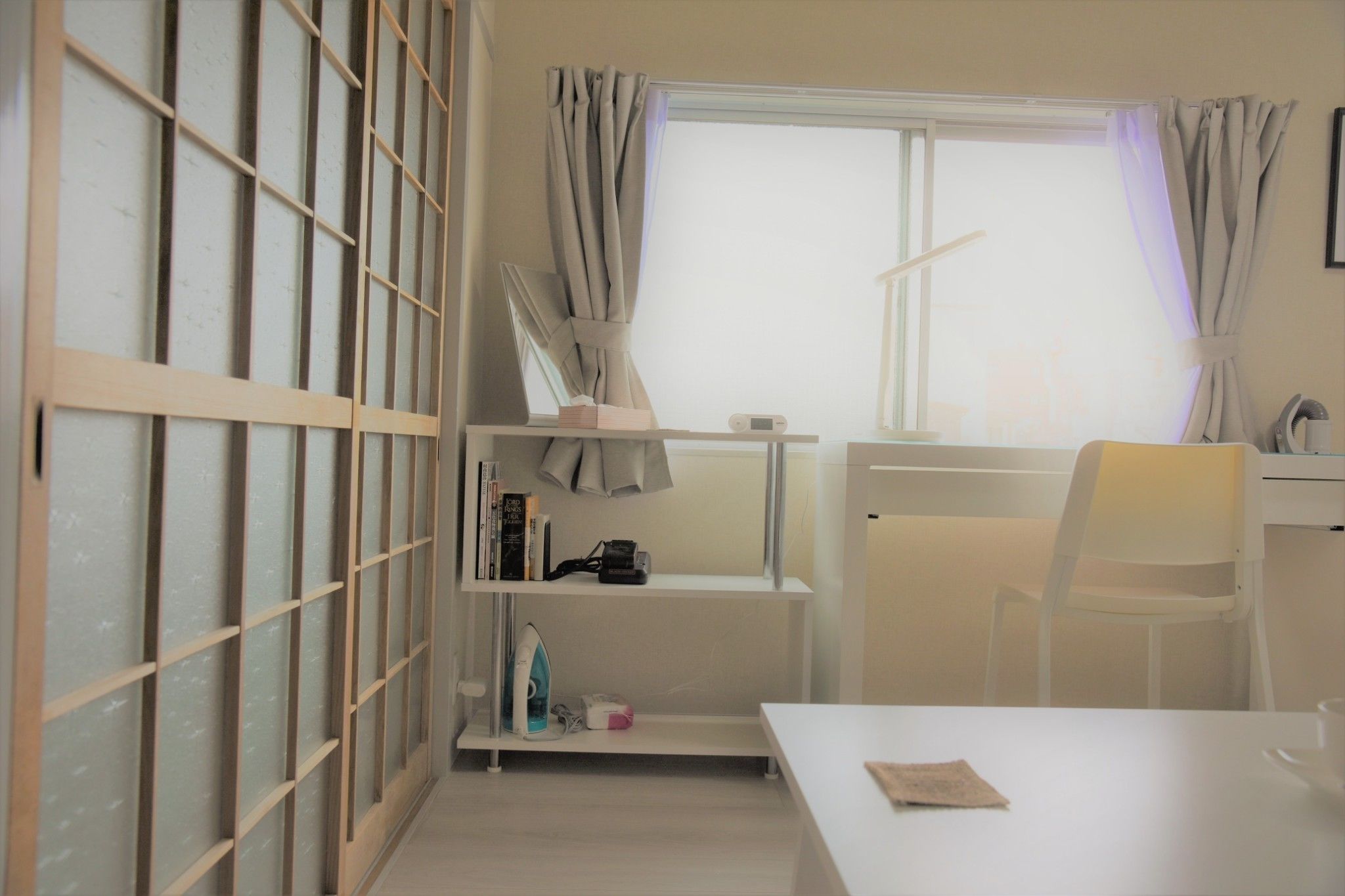Una habitación con un escritorio blanco, una silla y estanterías con libros y una cámara.