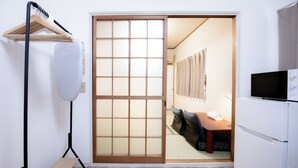 A room with a sliding shoji screen door, a wooden bench, a black floor lamp, a white refrigerator, and a television. - U-SHUKU Osaka (Osaka)