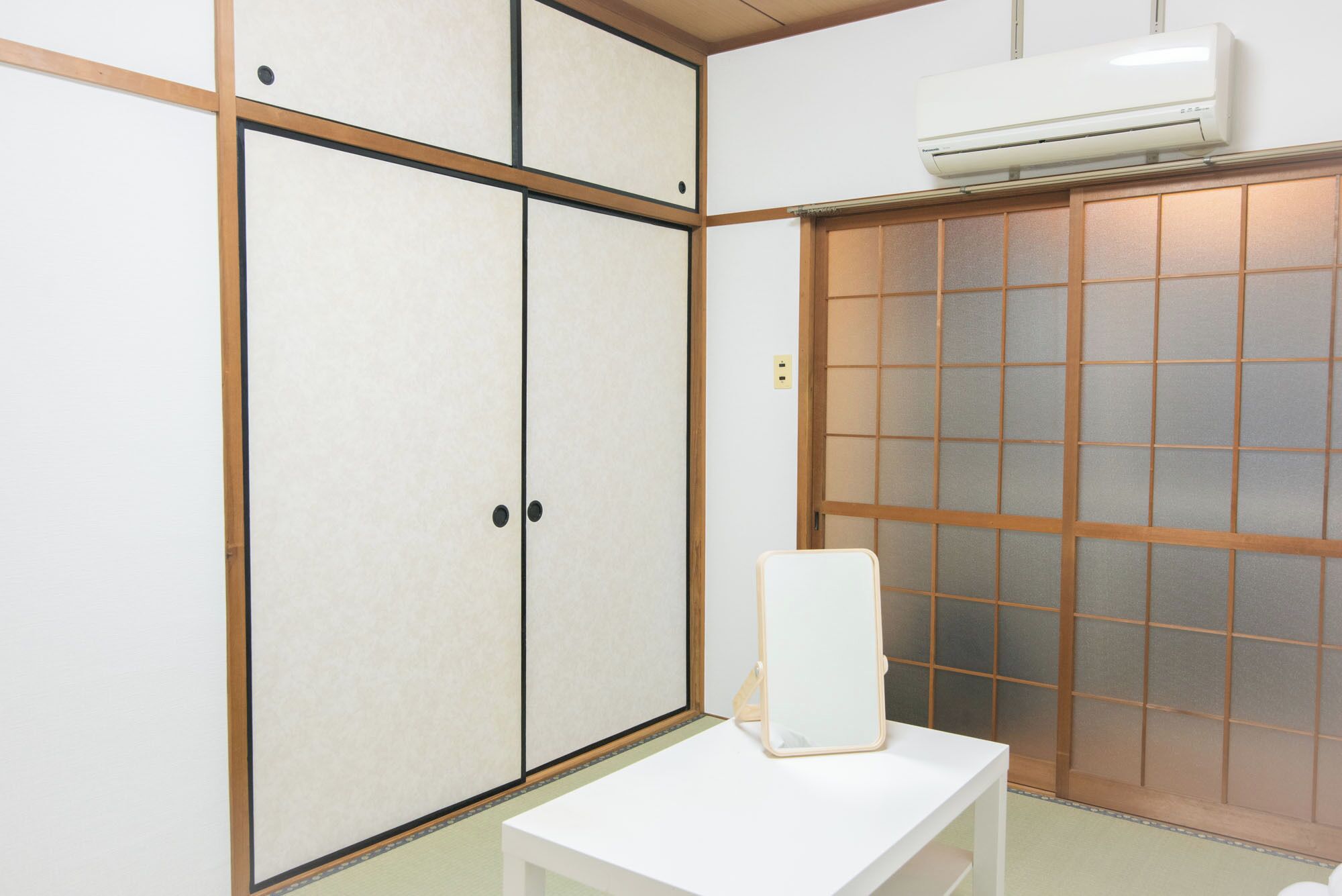Habitació amb porta corredissa d'estil shoji, una taula blanca i un aparell d'aire condicionat fixat a la paret.