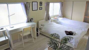 A hotel room with a bed, desk, chair, and a potted plant.