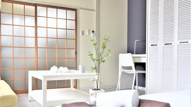 A modern hotel room with a sliding shoji screen door, a desk with a chair, a small potted plant, and a neatly made bed with a pink towel. - U-SHUKU Osaka (Osaka)