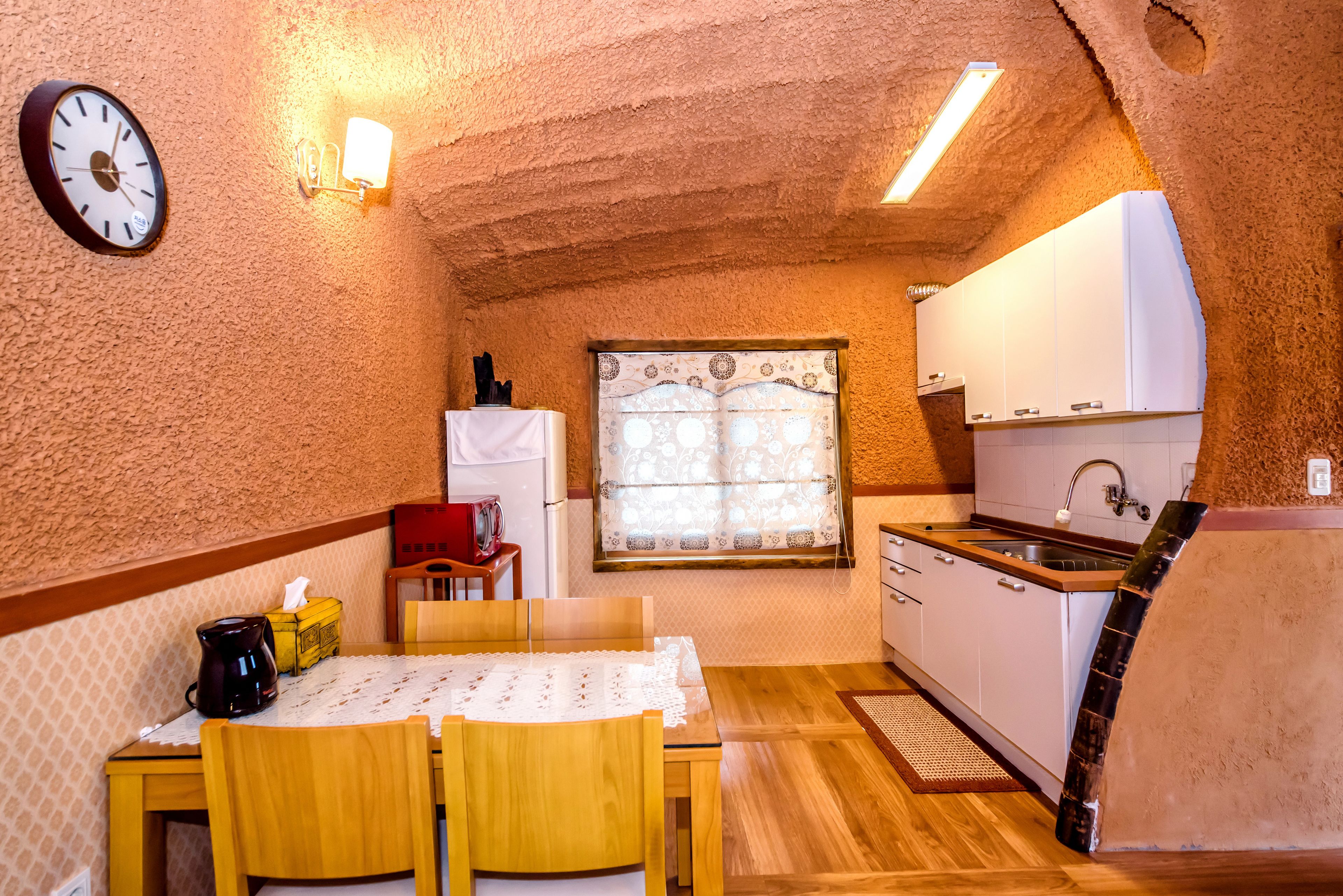 A compact kitchen with a wooden table, chairs, a coffee maker, and a refrigerator.