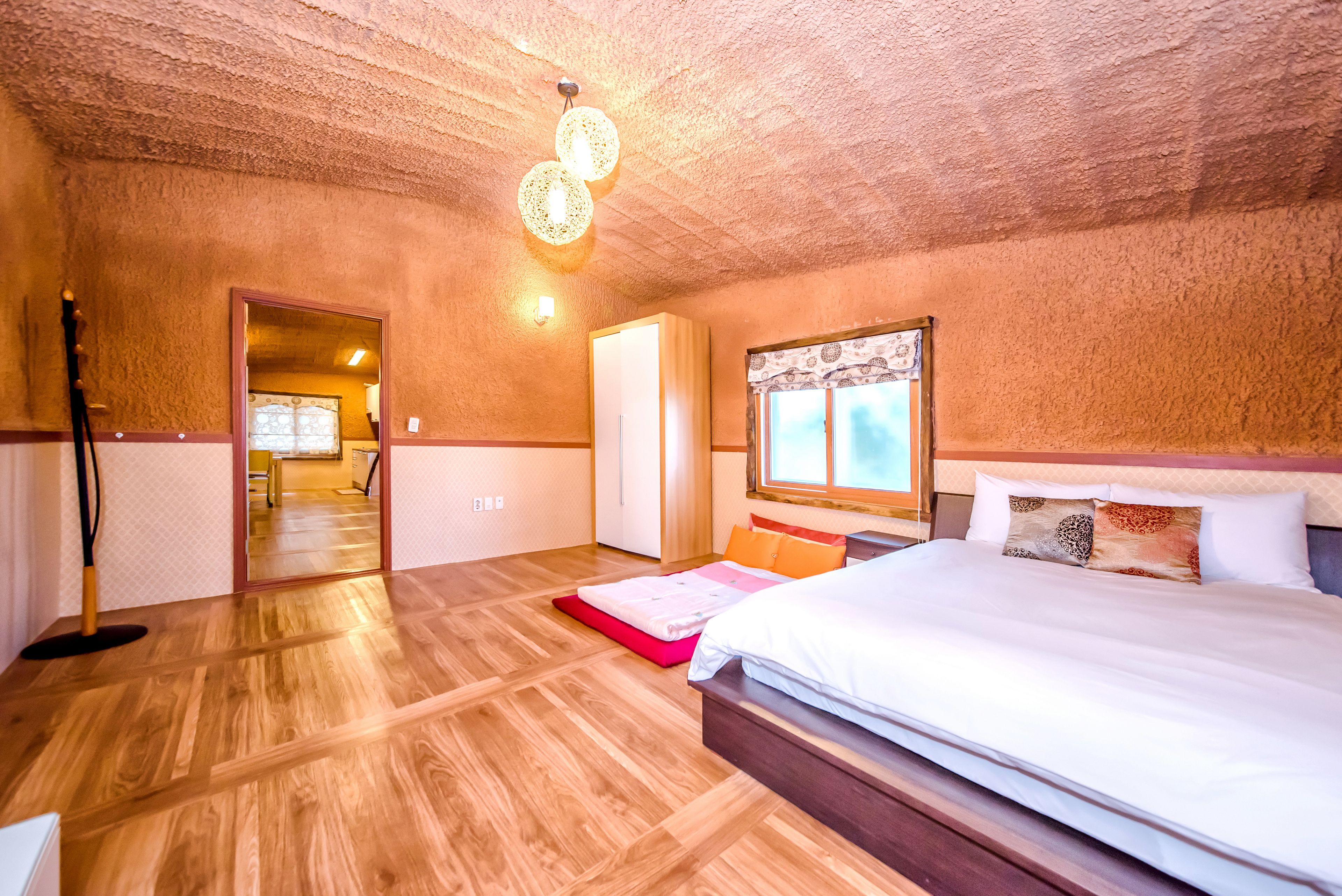 A bedroom with a wooden floor, a bed with white bedding, a wooden headboard, and a window with patterned curtains.