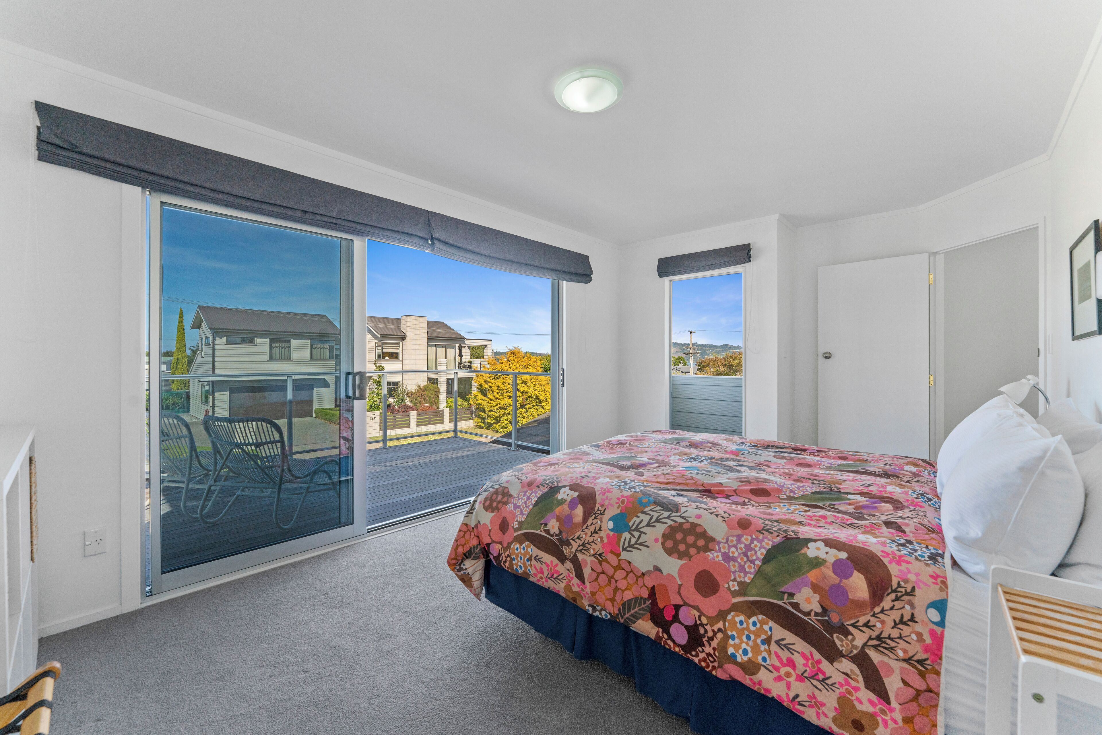 A bedroom with a large bed, a sliding glass door to a balcony, and a view of a house and trees.