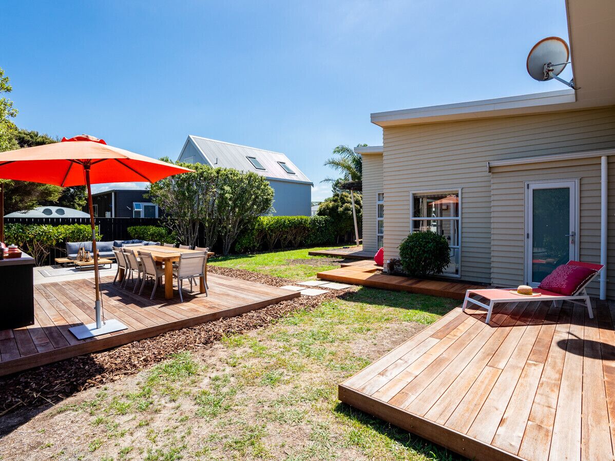 A backyard with a wooden deck, a dining table with chairs, a red umbrella, and a lounge chair.