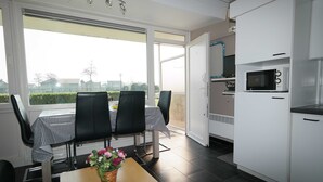 A modern kitchen with a microwave, a dining area with a table and chairs, and a view through large windows. - Park Atlantis (De Haan)