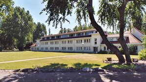 A large, multi-story building with a flat roof and a symmetrical facade, surrounded by a well-maintained lawn and trees. - Park Atlantis (De Haan)