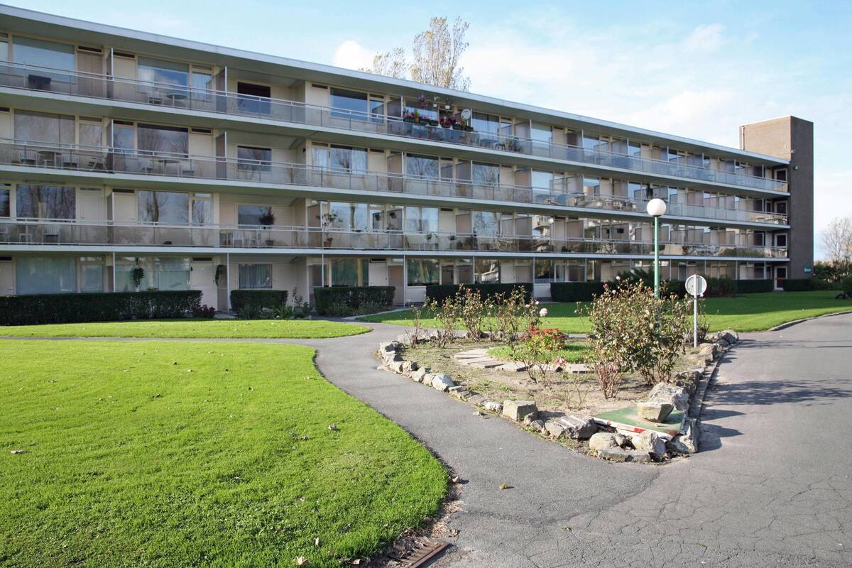 A multi-story residential building with balconies, a paved driveway, and a landscaped garden area.