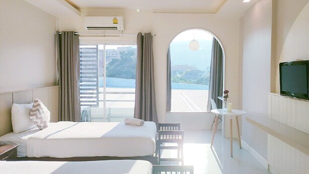 Quarto de hotel com cama, uma mesinha, televisão e vista para o exterior.