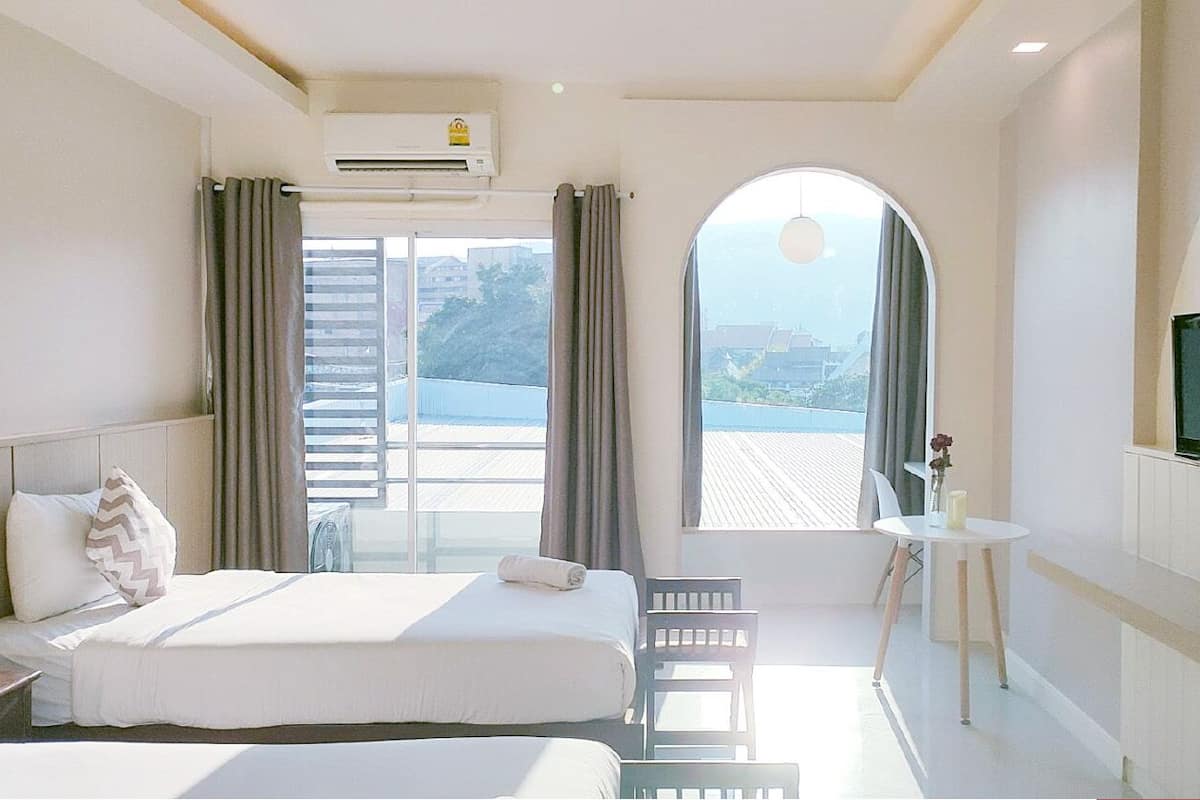 A hotel room with a bed, a small table, a TV, and a view of the outside.