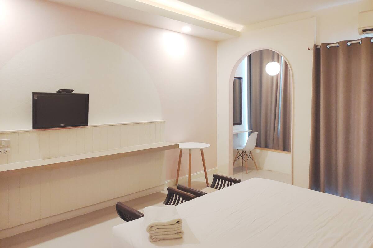 A hotel room with a bed, a small table, a chair, a TV on a shelf, and a mirror.