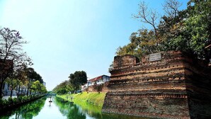 Um muro de tijolos históricos com uma placa, um canal e árvores.