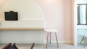 Quarto moderno com esquema de cores branco e rosa, televisão montada na parede, uma mesinha branca e uma cadeira.