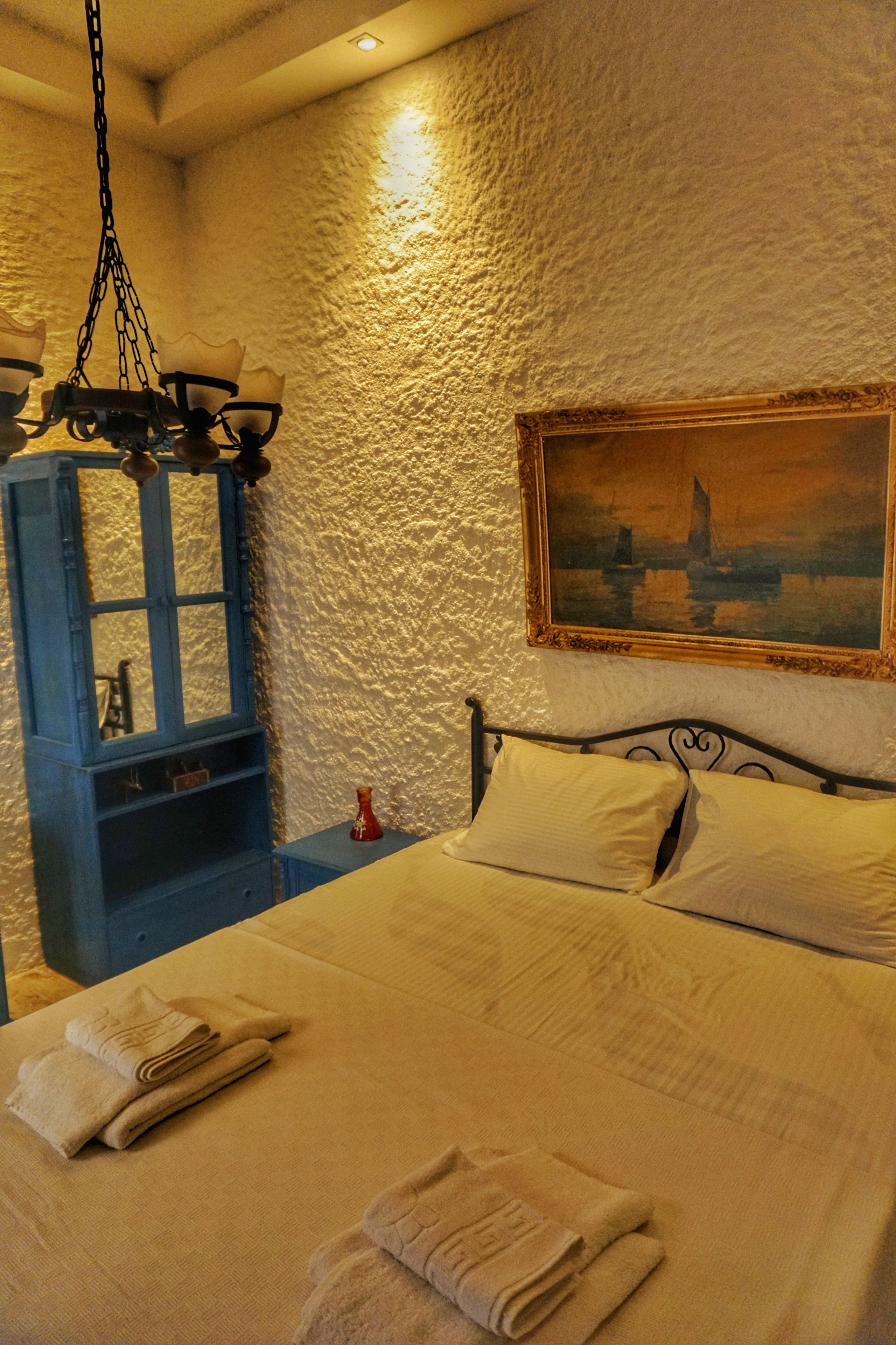A bedroom with a bed, a painting, a blue cabinet, and a chandelier.