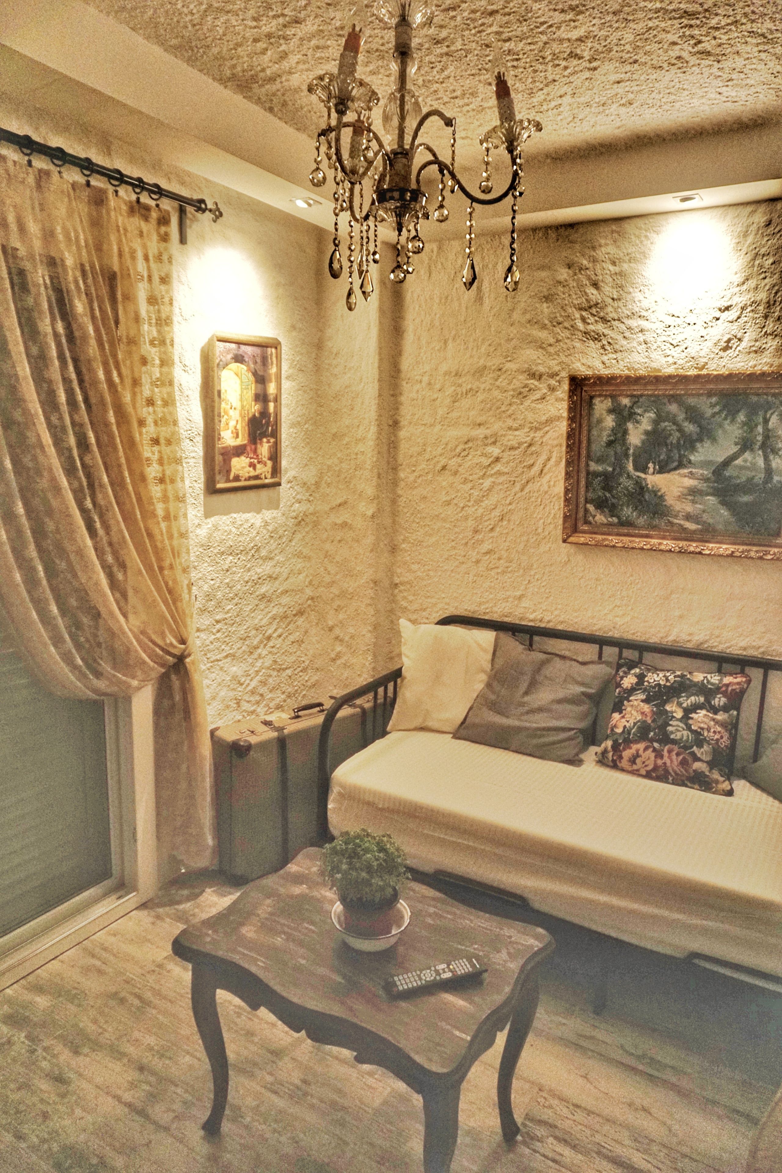 A cozy living room with a sofa, a wooden coffee table with a plant, a chandelier, and a painting on the wall.
