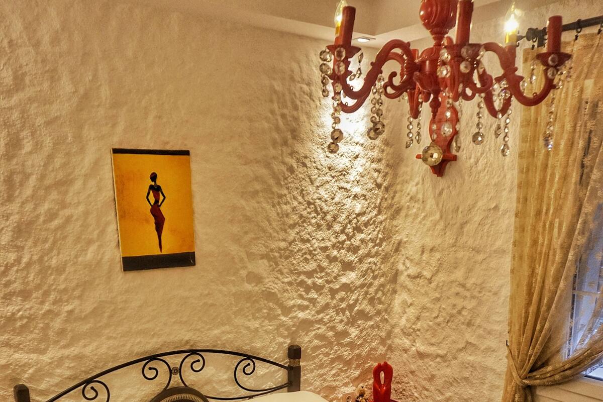 A neatly made bed with white linens and towels, a red nightstand with a red object on it, and a wall-mounted picture of a woman.