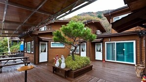A wooden cabin with a covered patio, a small garden with a tree, and a bench with snowman decorations. - Jirisan Shiri Pension (Gurye)
