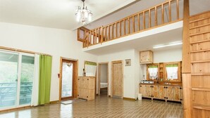 A spacious room with a wooden floor, a balcony with a wooden railing, and a large window with green curtains. - Jirisan Shiri Pension (Gurye)