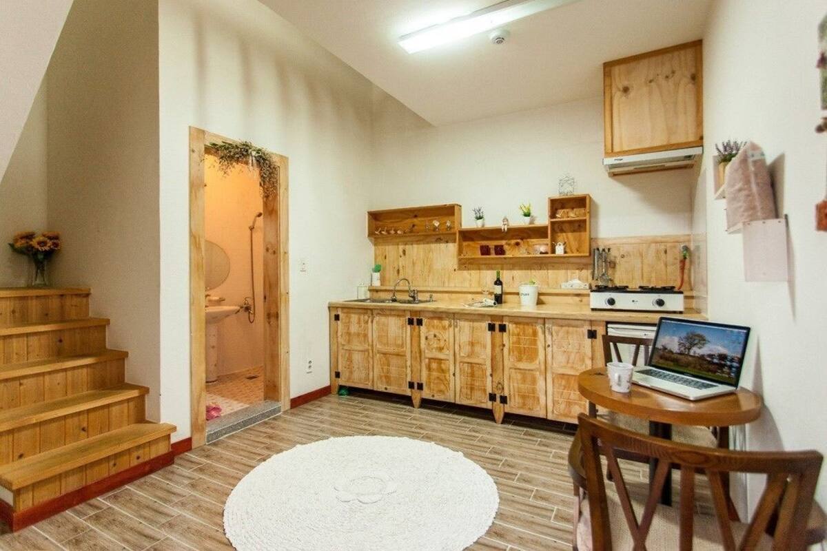 Eine kleine Küche mit Holzausstattung, ein Laptop auf einem Tisch und eine Treppe, die zu einem Badezimmer führt.