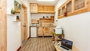 A compact kitchen with wooden cabinets, a small refrigerator, and a laptop on a table. - Jirisan Shiri Pension (Gurye)