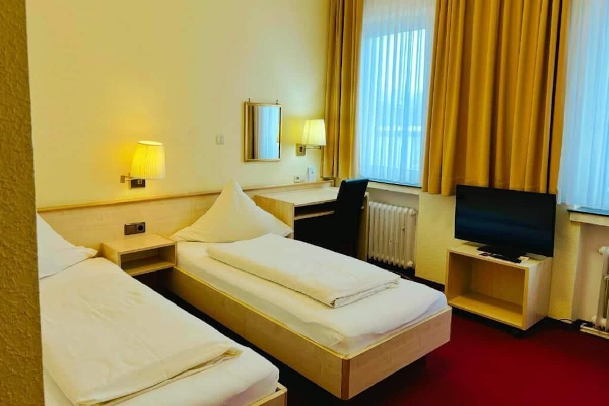 Habitación de hotel con dos camas, un escritorio, una silla, un televisor y una ventana con cortinas.