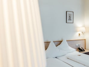 Habitación de hotel con cama, lámpara de noche, teléfono y un cuadro en la pared.