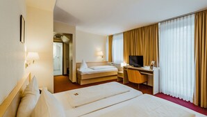 Una habitación de hotel con una cama grande, un escritorio con silla, televisión y ventana con cortinas.